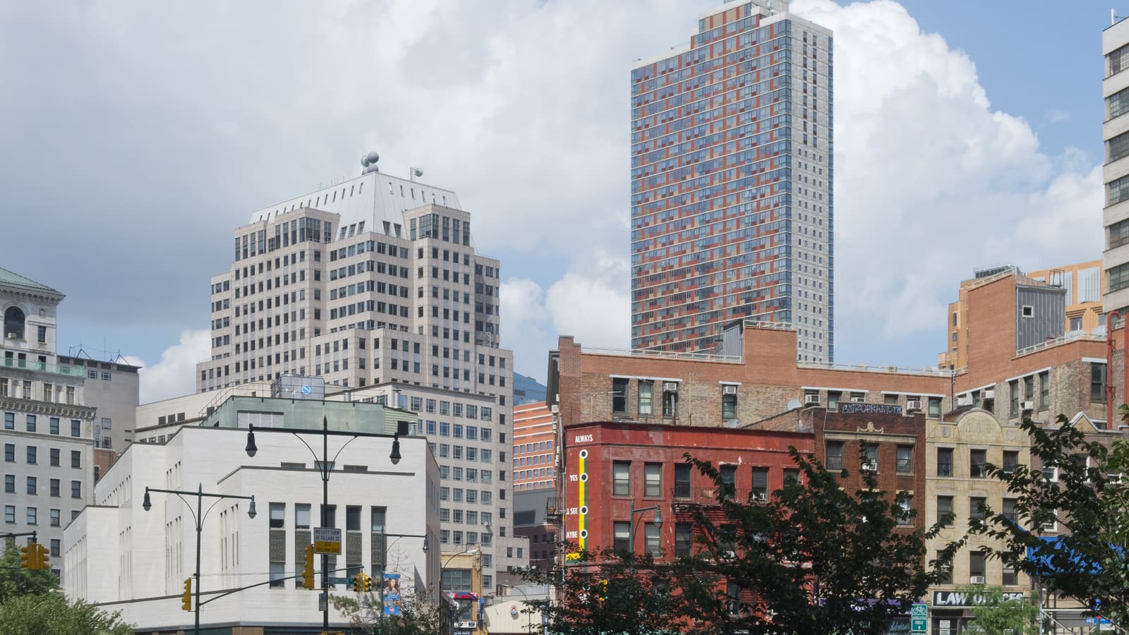 Office towers and older brick walk-up buildings in Downtown Brooklyn under a cloudy sky.