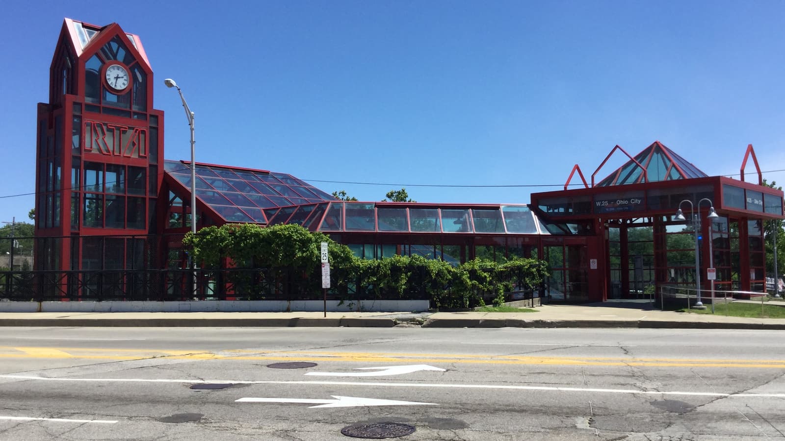 Red steel and glass rail station with a clock tower lettered RTA and a canopy lettered W. 25 - Ohio City, seen from across a street
