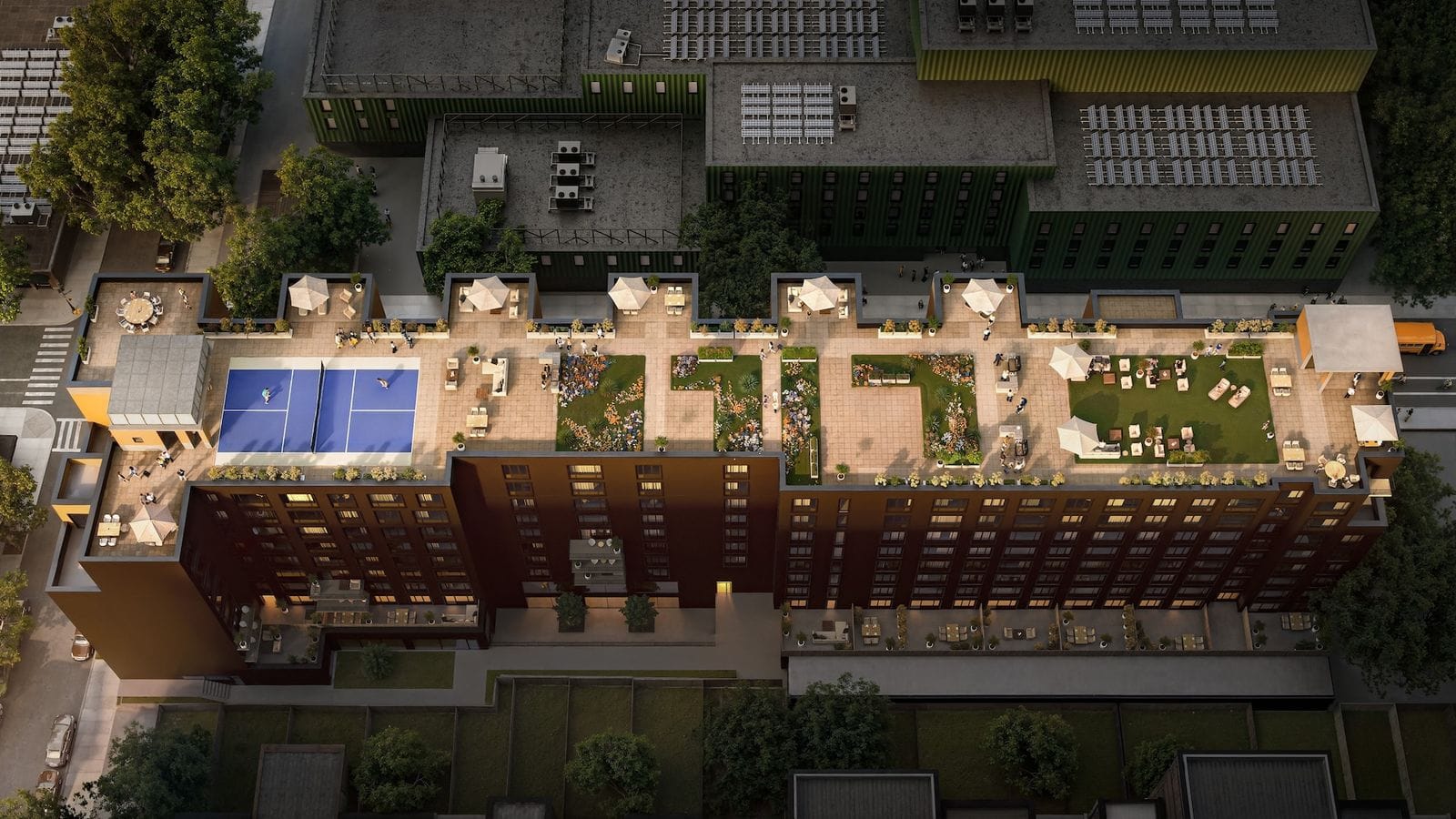 Rendering seen from high above at dusk of a long brick building's roof, with a blue pickleball court, planted beds, lawn areas, umbrellas, tables and lounge chairs, beside larger dark green buildings with solar panels on their roofs