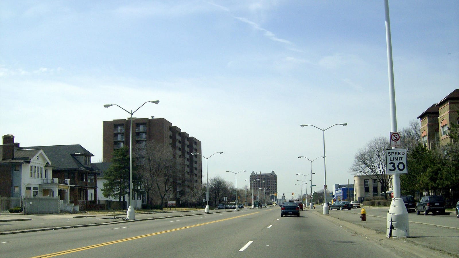 Photograph looking along a wide boulevard with houses and an apartment block on the left, street lamps down the median and a tall tower in the far distance