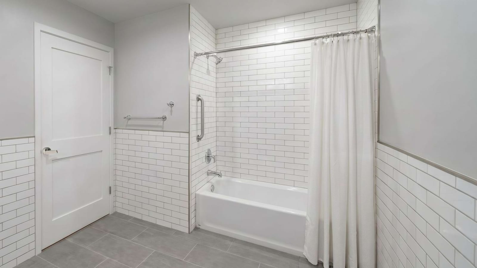 Rendering of a bathroom with white subway tile, a bathtub with a shower curtain, grab bars and a gray tile floor