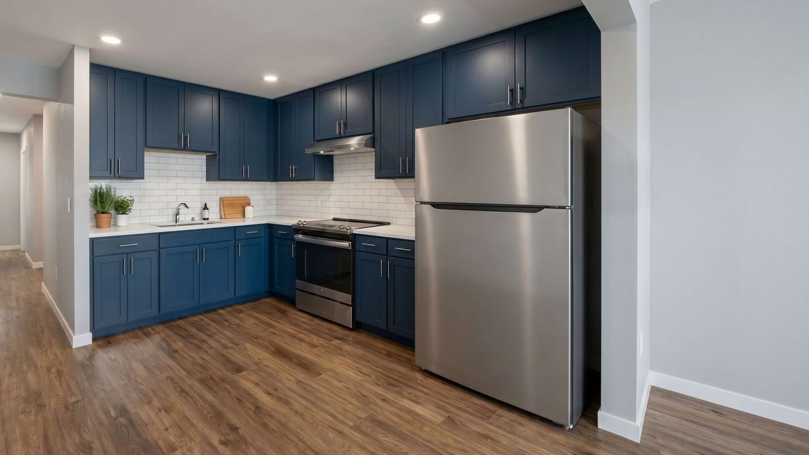 Rendering of a kitchen with navy blue cabinets, white subway tile, a stainless steel refrigerator and an electric range on a wood-look floor