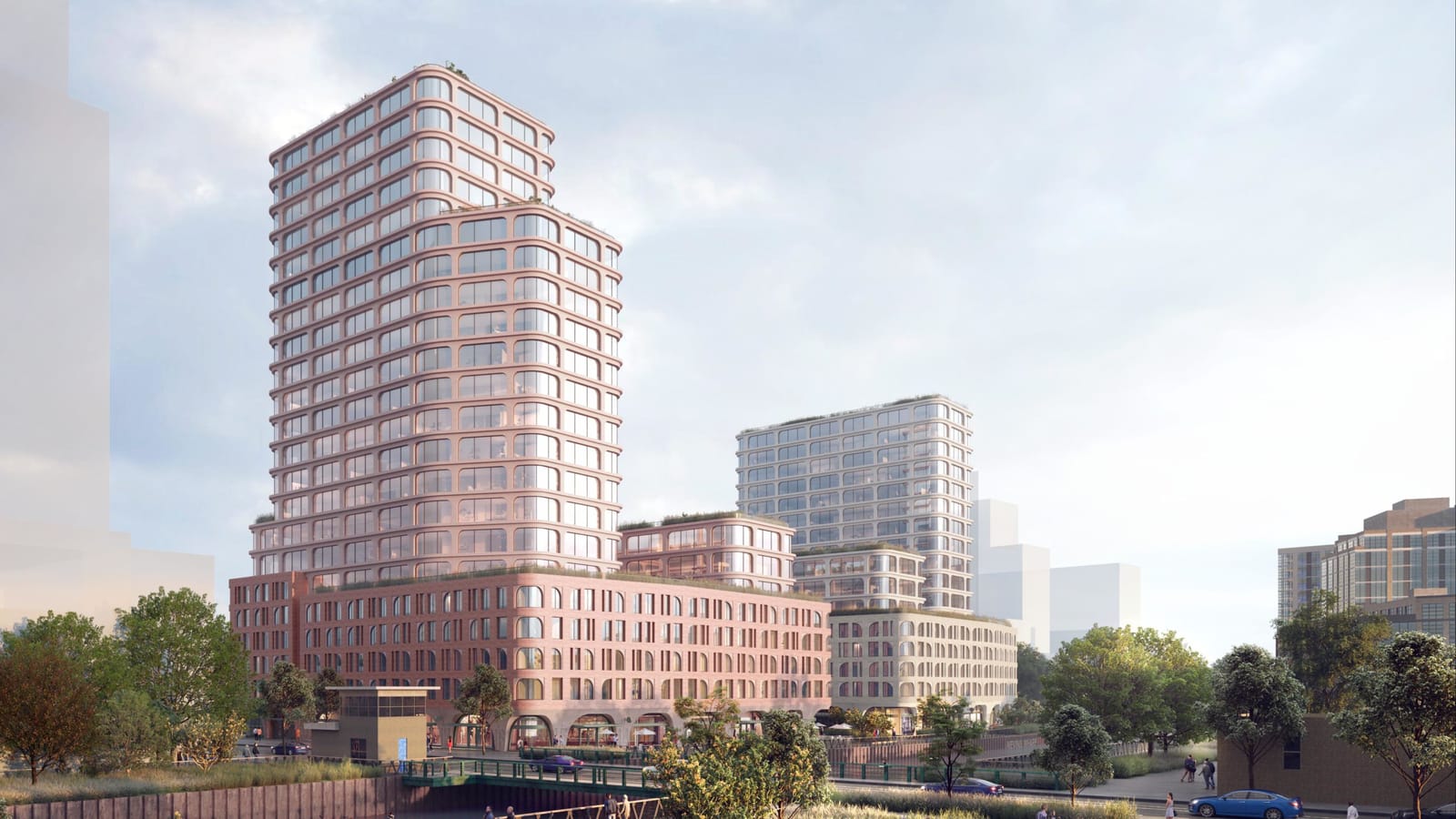 Rendering of a tall tower with rounded window bays in a red-pink tone rising from a wide red-brick base beside a canal and a small bridge, with a much lower pale tower on a pale base behind it at the right, trees along the water and cars on the street in the foreground