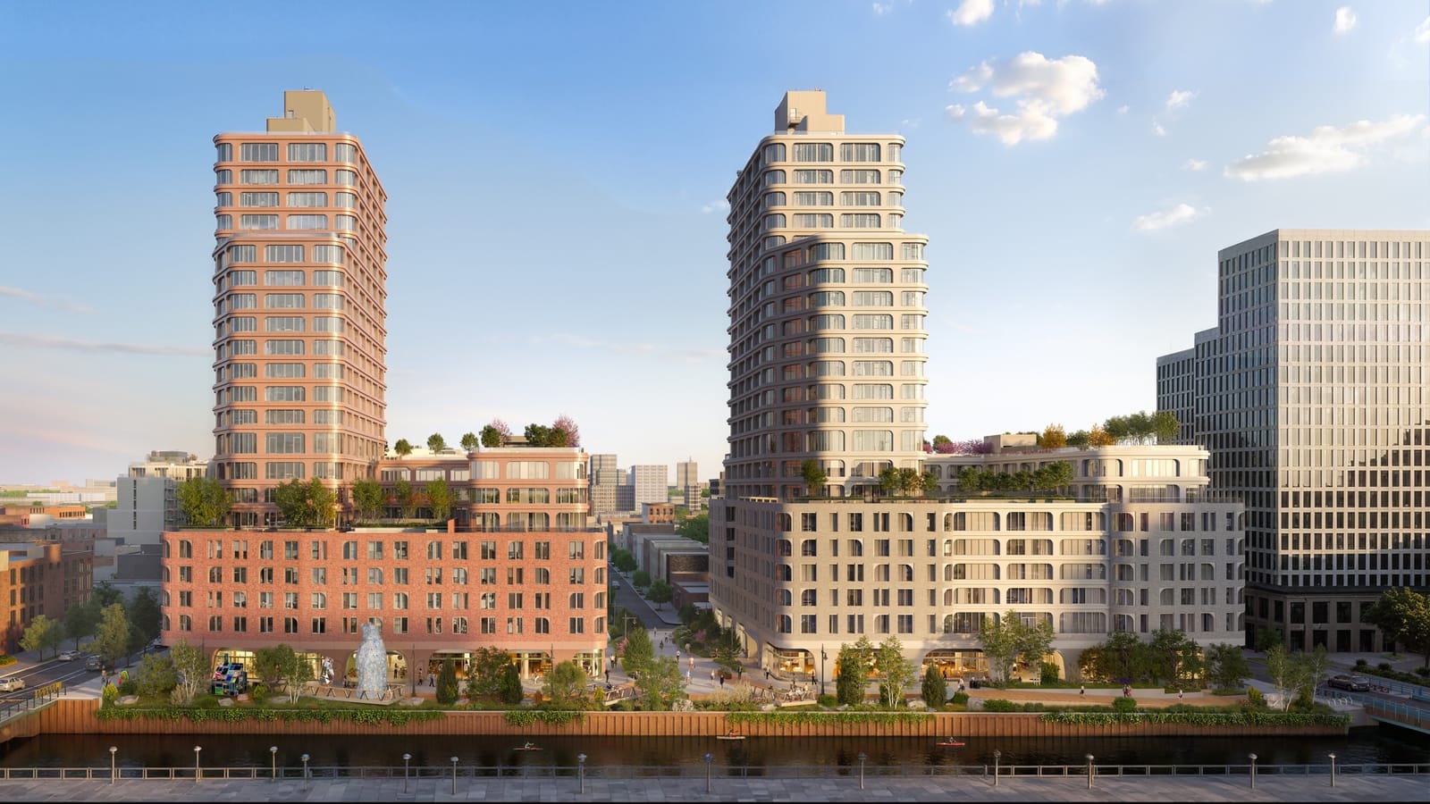 Rendering of two apartment towers on the bank of a canal: at left a tower rising from a wide base of red brick, at right a tower rising from a wide base of pale grey brick with arched windows, both with planted terraces on the roofs of their bases; a planted walkway with trees, seating and a tall blue bear sculpture runs along the bulkhead, kayakers are on the water, and a glass building with a square grid of windows stands at the far right