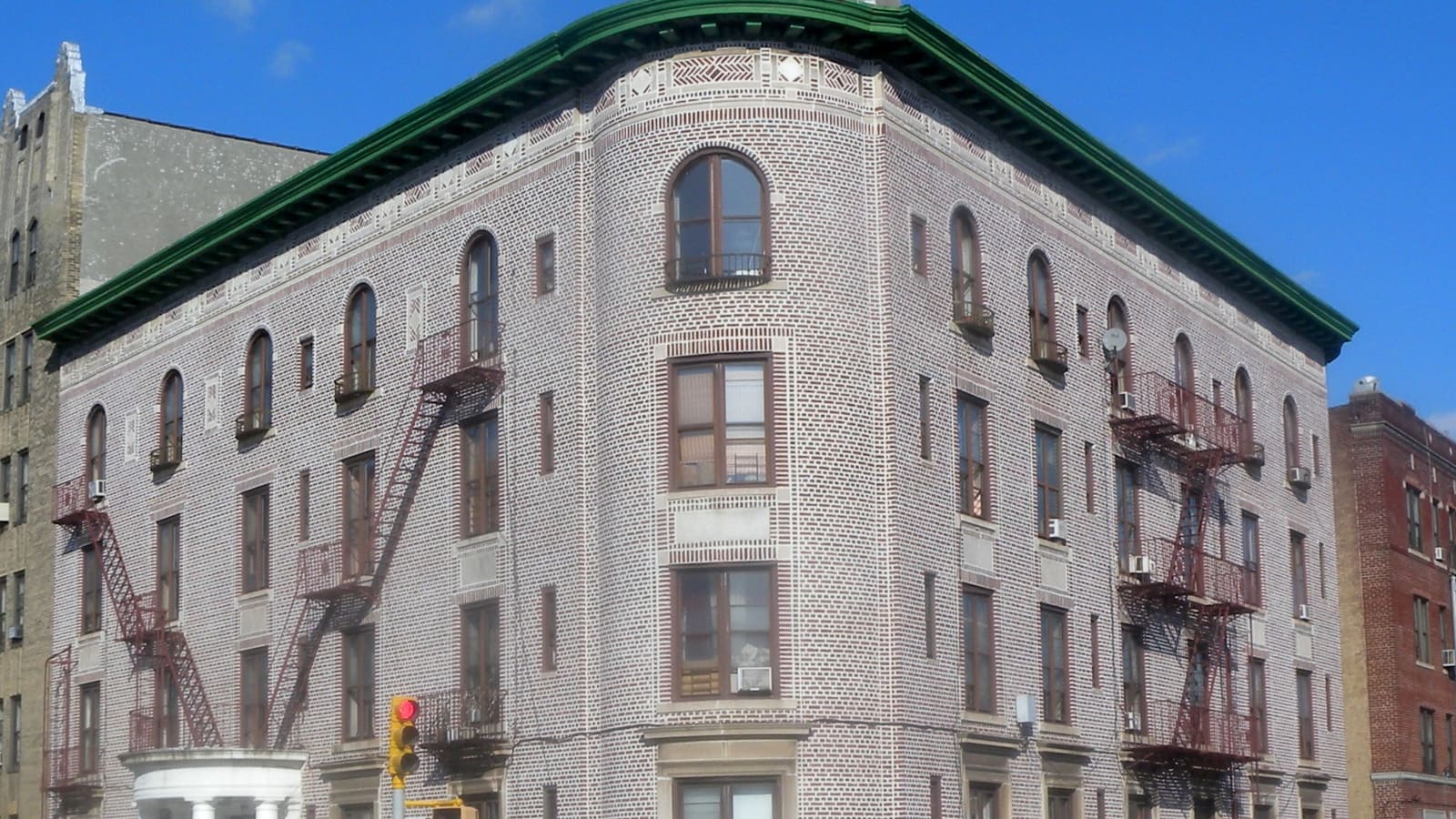 A six-story brick apartment house with green trim on a street corner