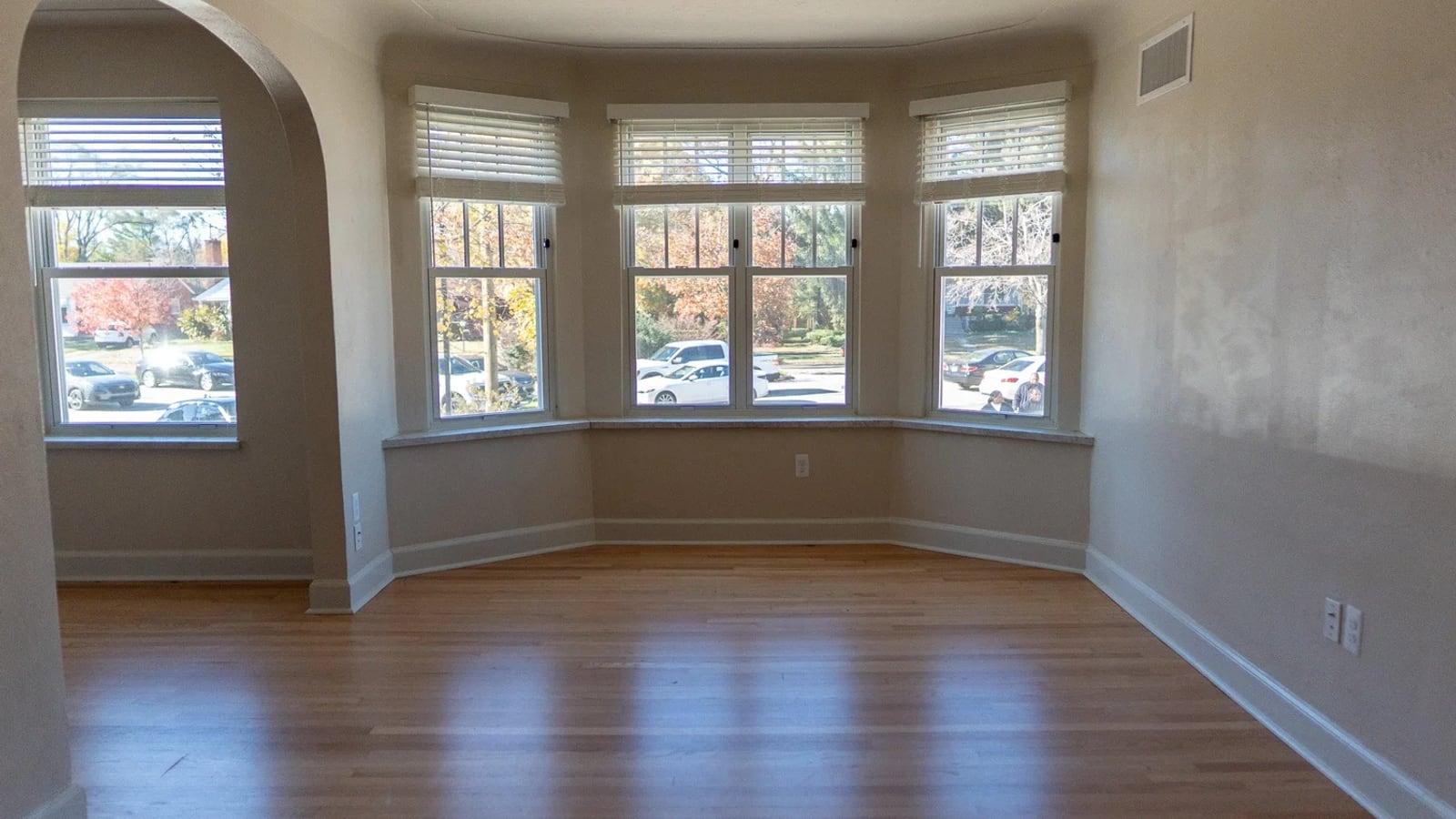 Photograph of an empty room with a wood floor, an arched opening and a bay of four windows with blinds