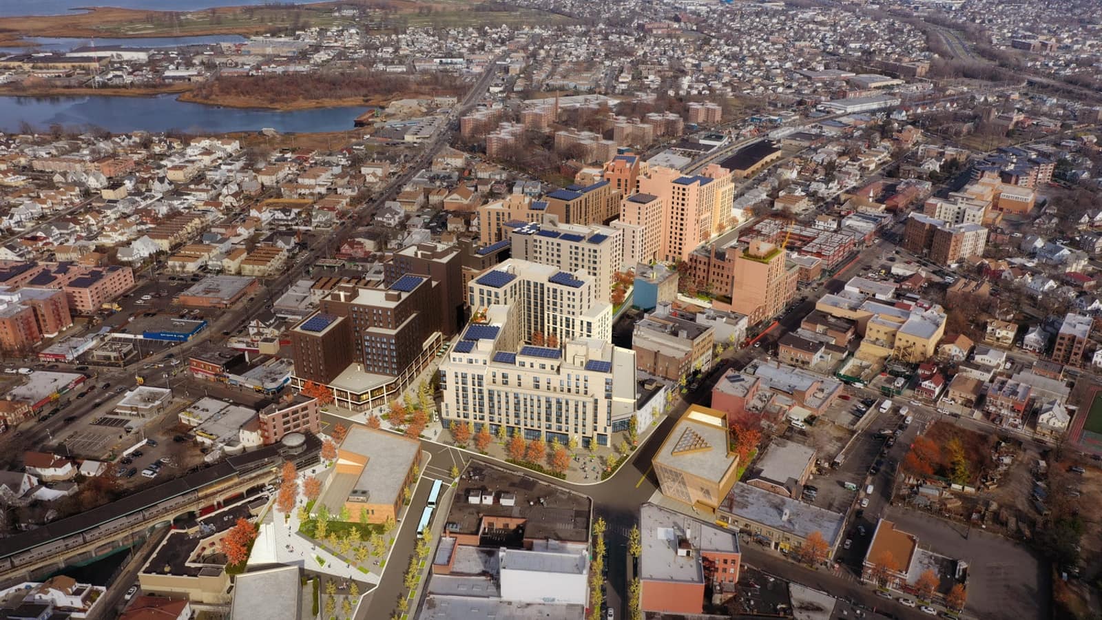 Aerial rendering of a cluster of new mid-rise apartment buildings in white, tan and dark brown with solar panels on their roofs, set among low houses and older brick apartment blocks, with an elevated train line at lower left and marshland and water in the distance