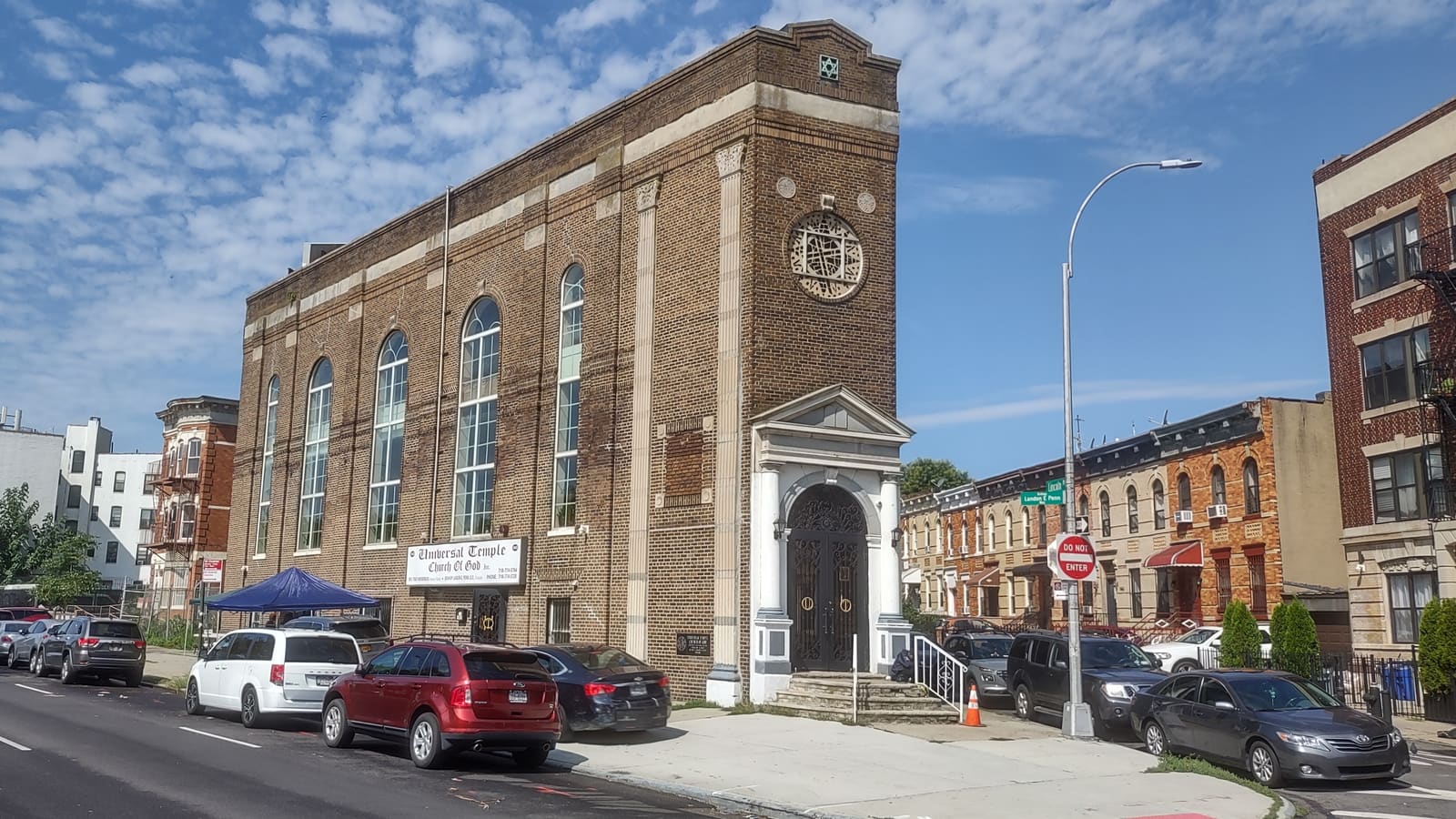 A narrow brick building with tall arched windows on a corner, with row houses beside it