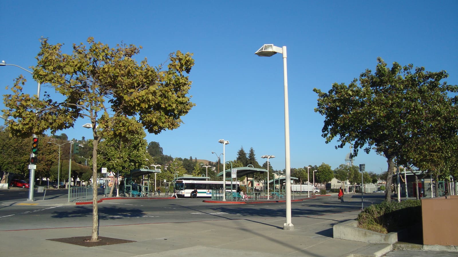 Bus shelters and an AC Transit bus at a transit center, with trees in front and hills behind