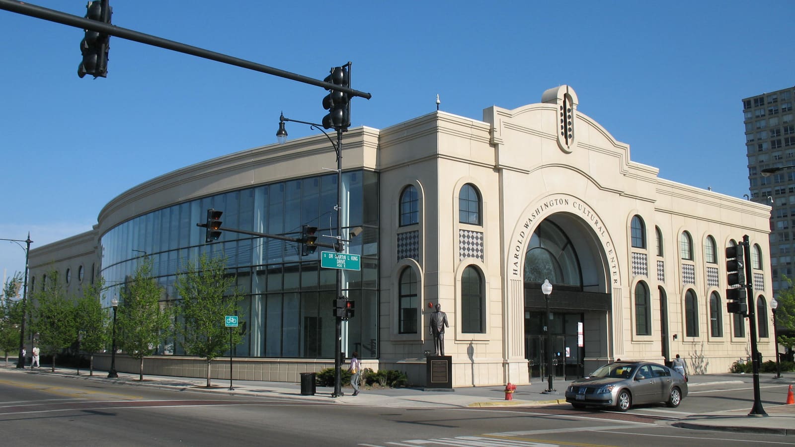 A cream stone building with an arched entrance and a curved glass wall on a street corner, its name carved over the door