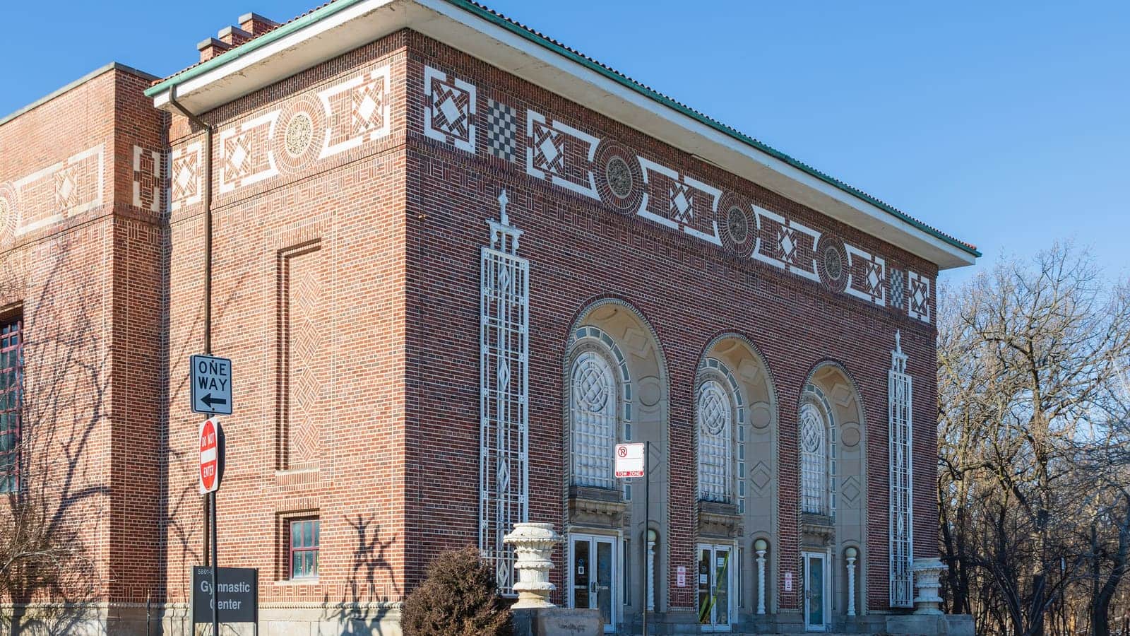 A red brick building with patterned brick and terracotta bands, three tall arched windows over its doors and a sign reading Gymnastic Center
