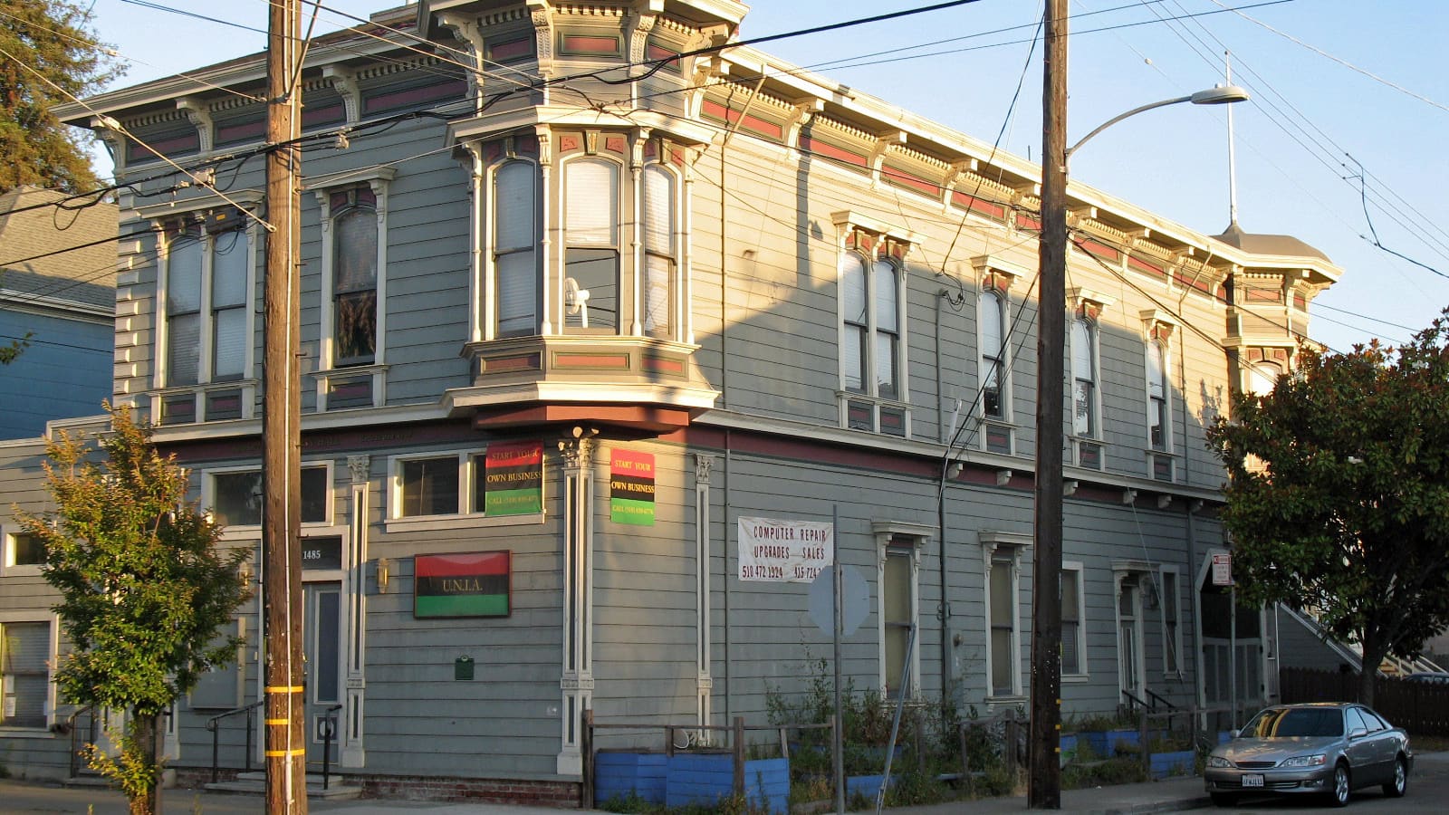 A two-storey grey Victorian wooden building with a corner bay window and bracketed cornice at a street corner