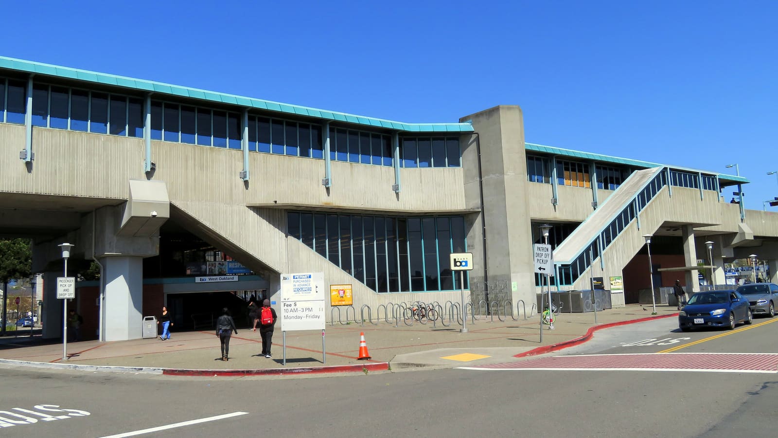 The concrete elevated West Oakland BART station with its street-level entrance, bike racks and a station sign