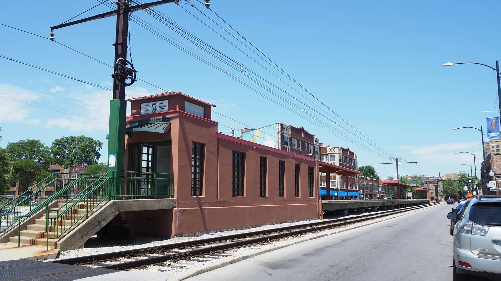 A small terracotta-coloured station building with a South Shore sign beside a single railway track running along a street lined with brick apartment buildings