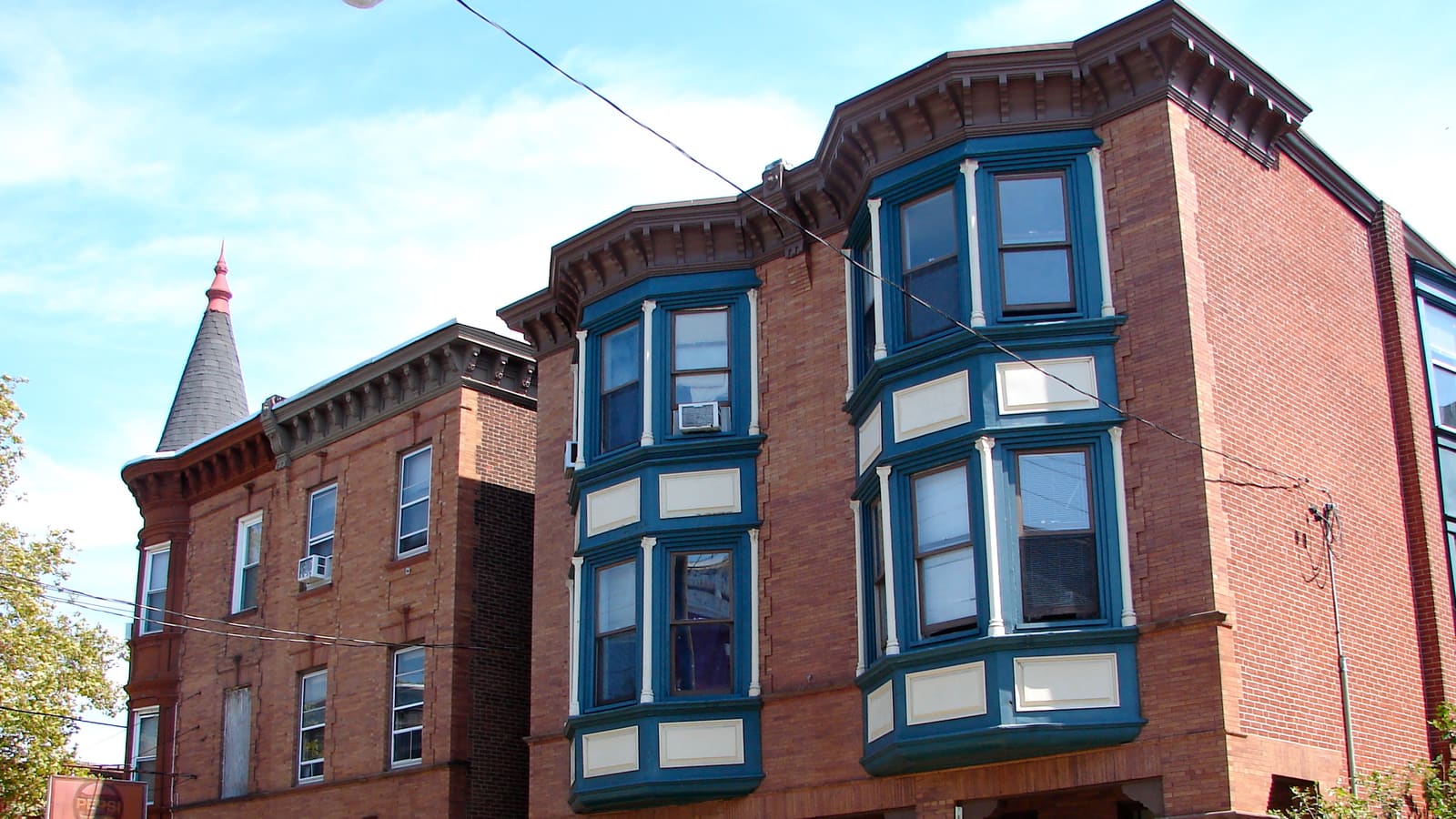 Three-storey red brick houses with blue and cream bay windows and bracketed cornices, beside a brick building with a conical slate turret
