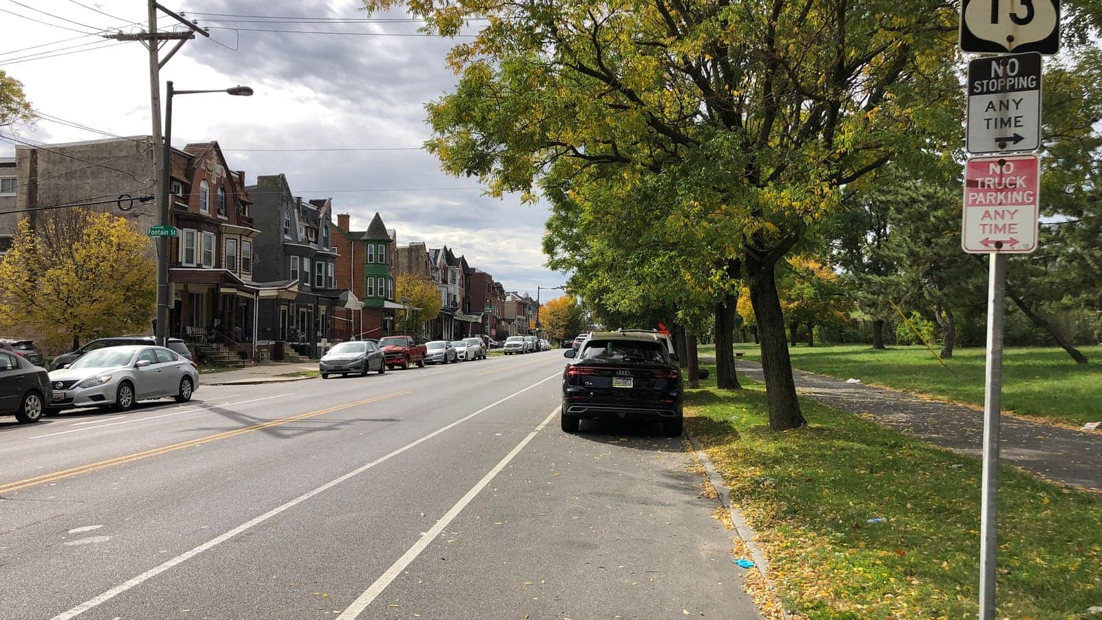 A wide street with three-storey rowhouses on the left and the trees and lawn of a park on the right, and a Fontain St sign at the corner