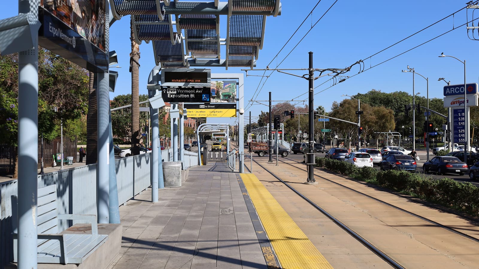 A light rail platform with a sign reading Expo/Vermont and an exit sign for Vermont Av and Exposition Bl, beside a busy intersection