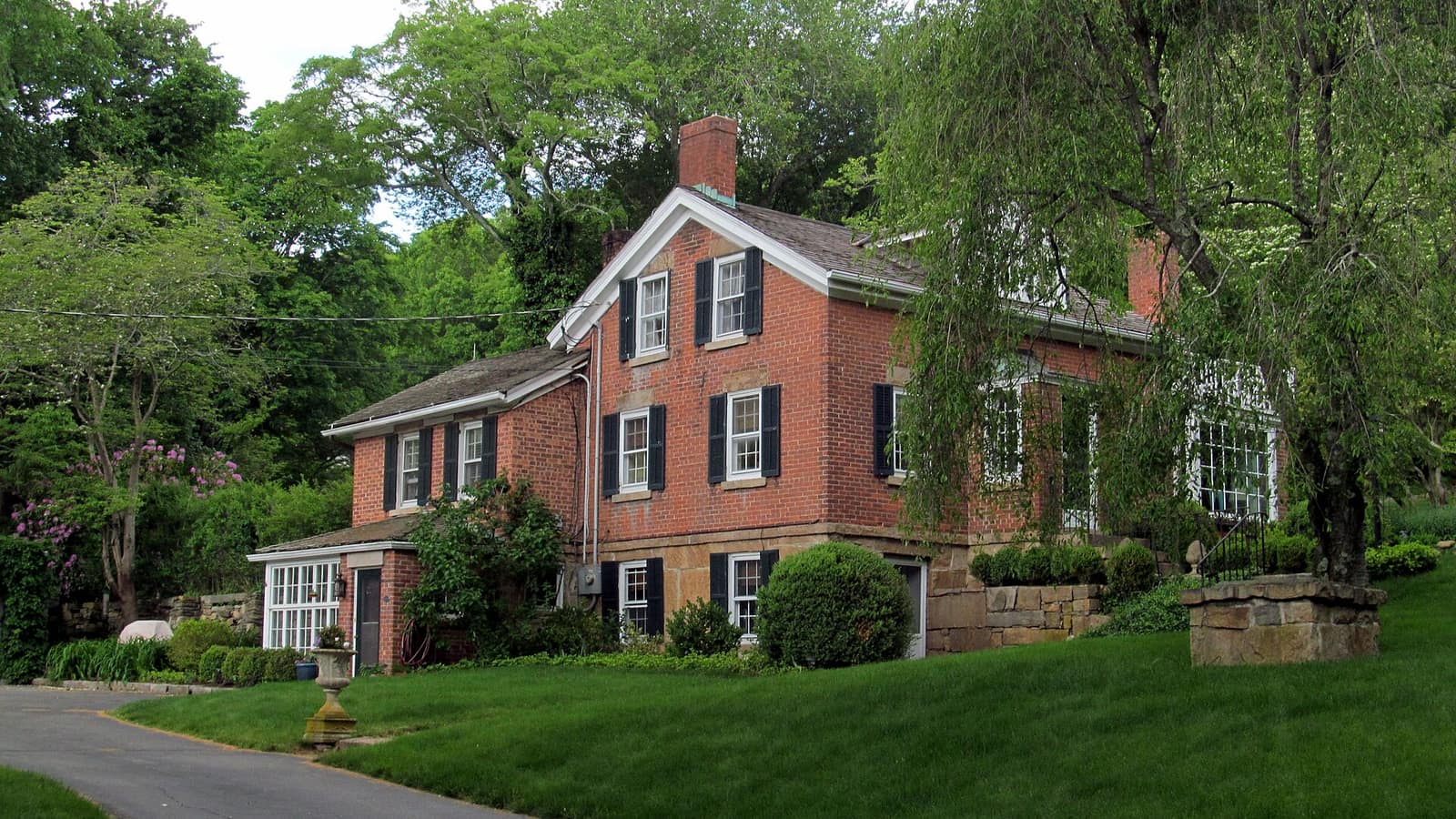 Red house with white trim amid trees and a green lawn