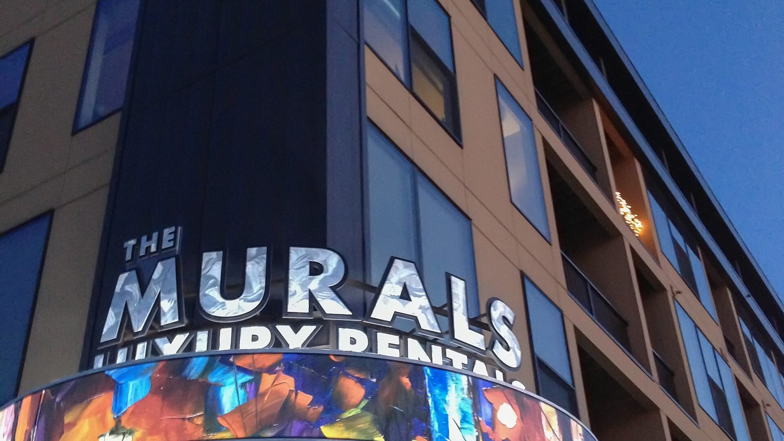 Apartment facade with a colorful mural and large building sign