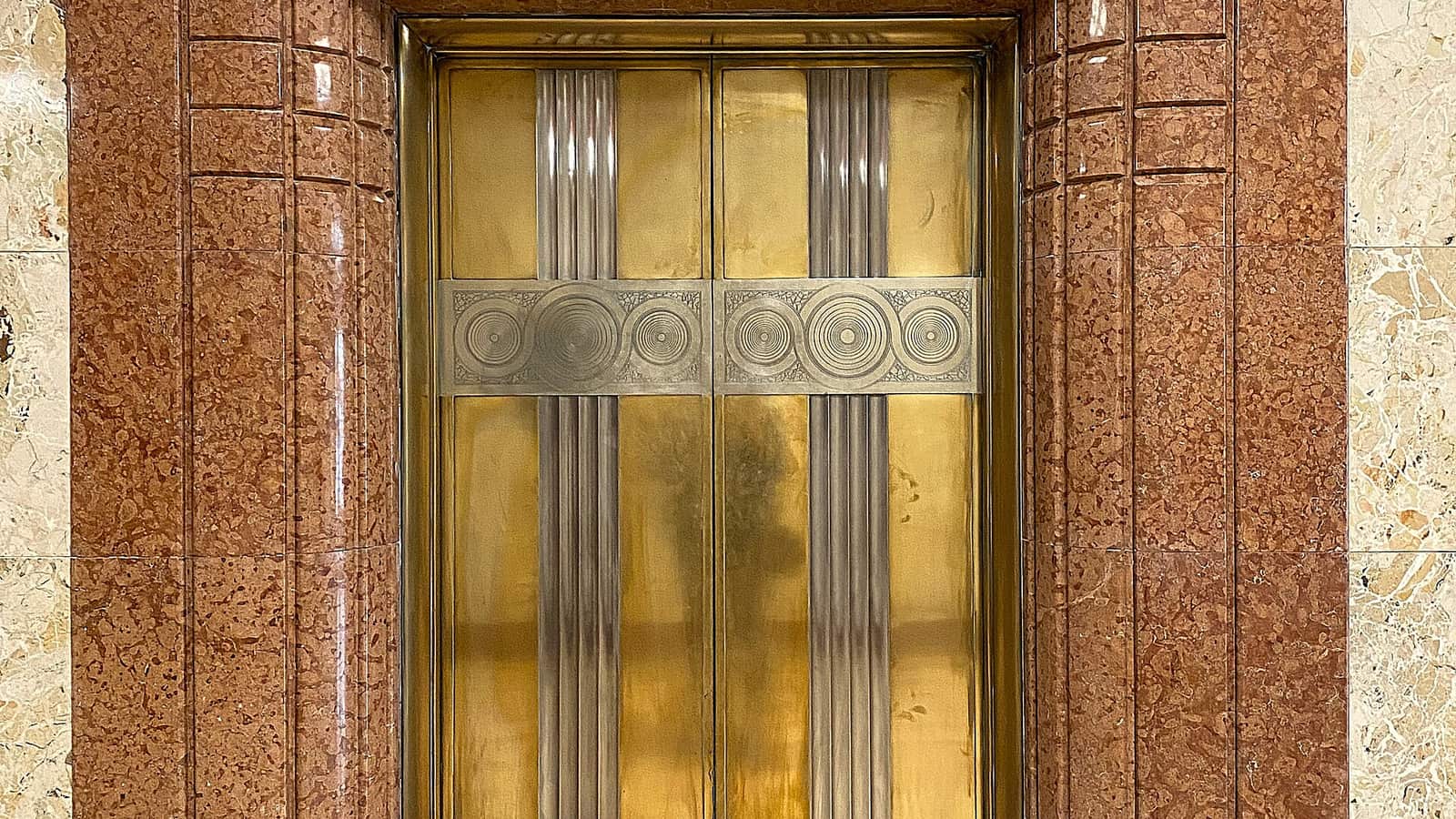 Decorative metallic elevator doors inside a stone-lined lobby