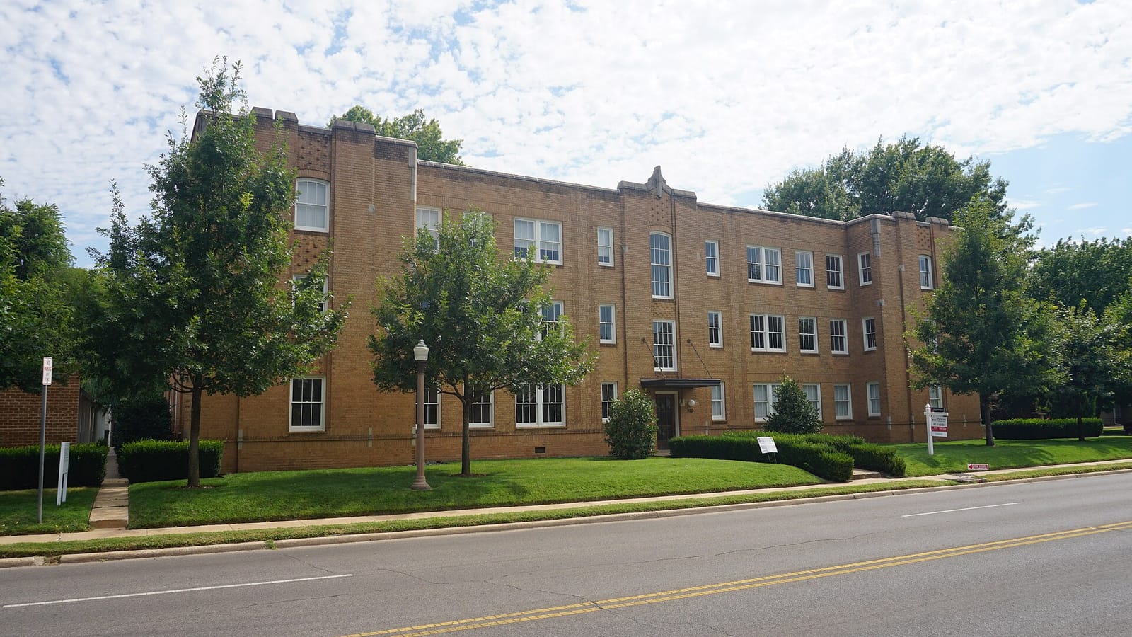 Tan brick apartment building beside a lawn and street