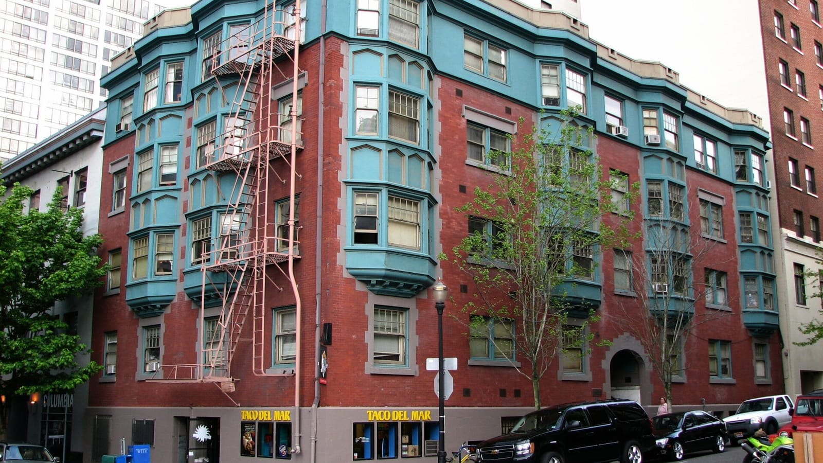 Red brick apartment building with turquoise window bays and fire escapes
