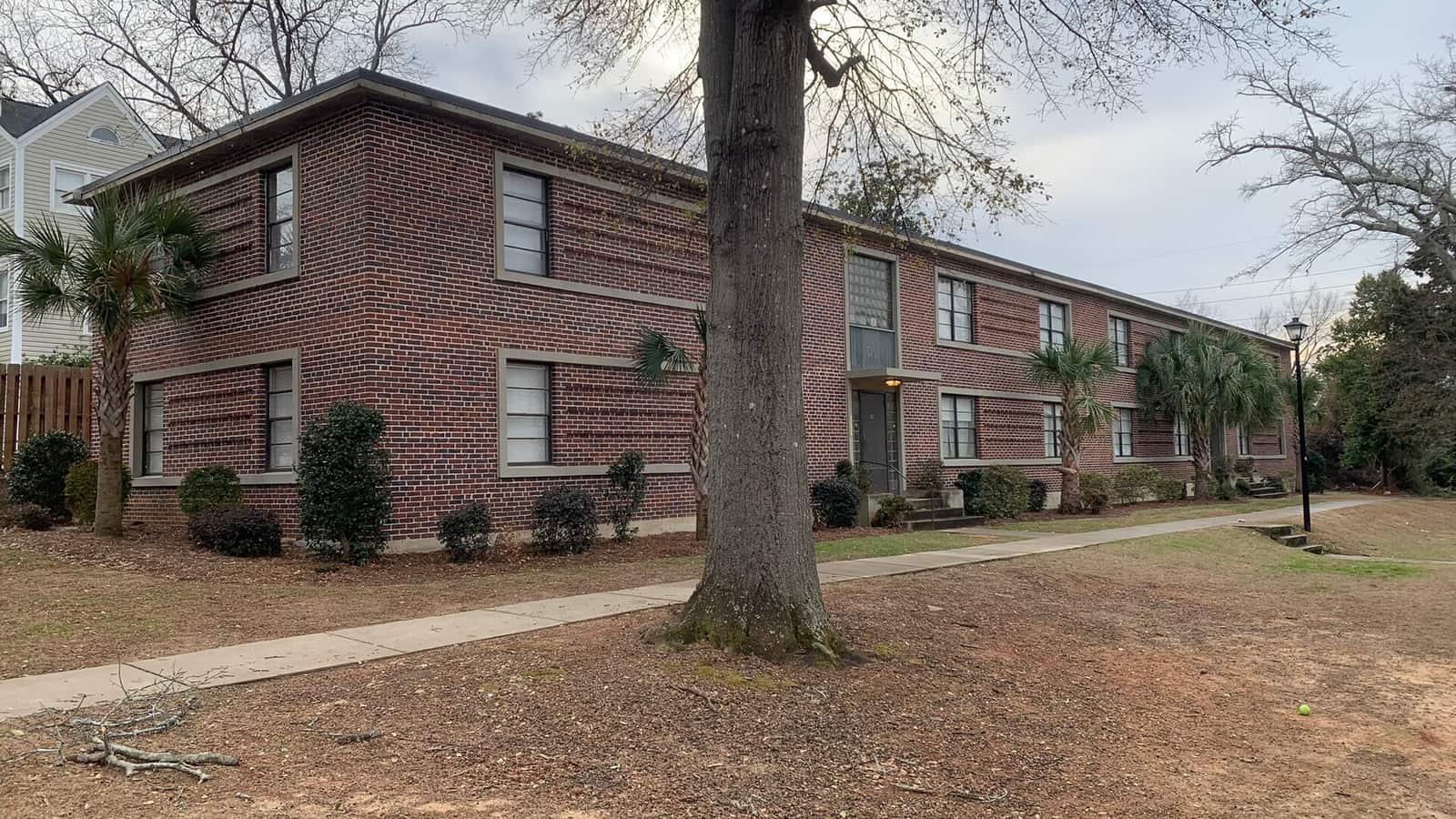 Two-story brick apartments beside a lawn and trees