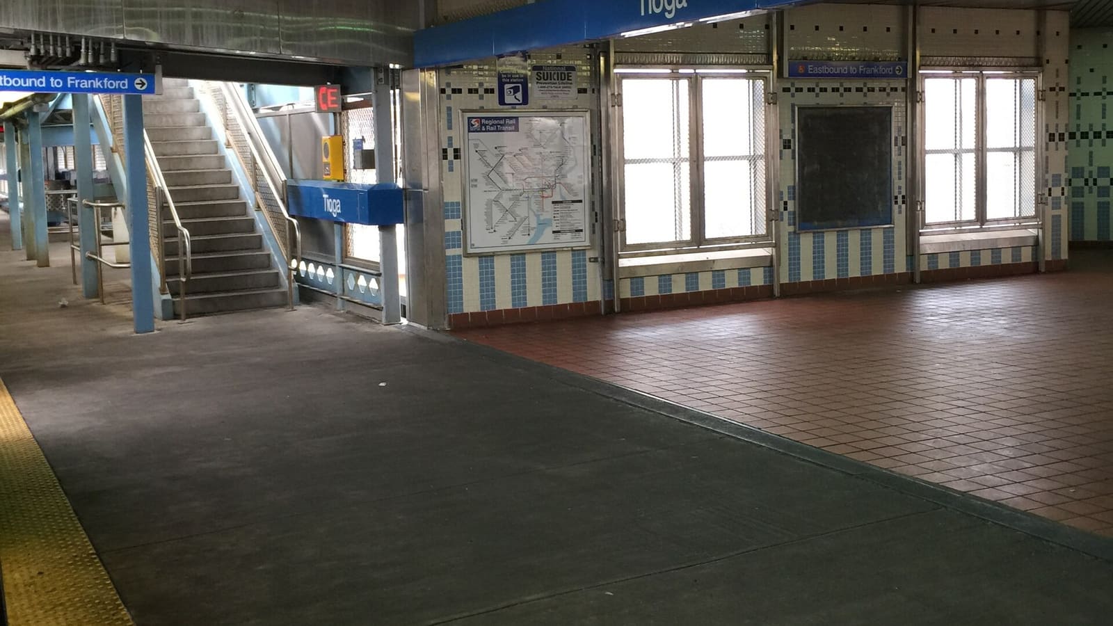 Elevated station platform with blue and white tile walls, a blue sign reading Tioga, a system map, a stairway and a sign for eastbound trains to Frankford