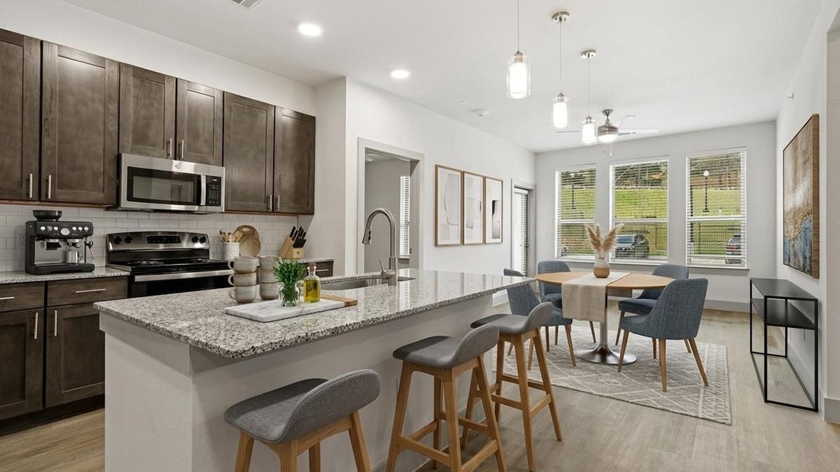 Kitchen with dark cabinets, stainless steel appliances and a granite island with three stools, beside a dining table and windows