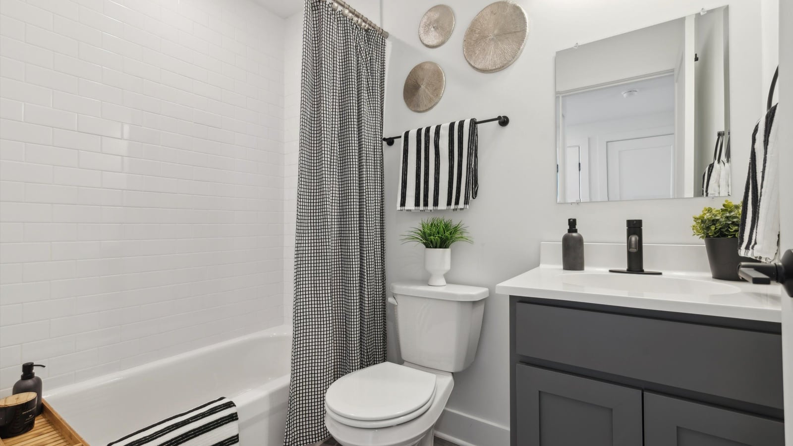 Bathroom with a bathtub behind a checked shower curtain, white subway tile, a toilet, and a dark gray vanity with a white top and a mirror