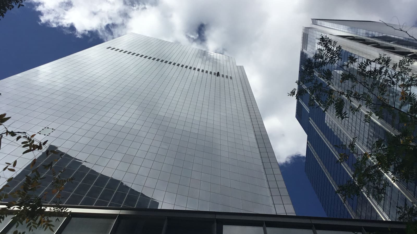 Looking up at a glass office tower reflecting clouds, with a second tower to the right