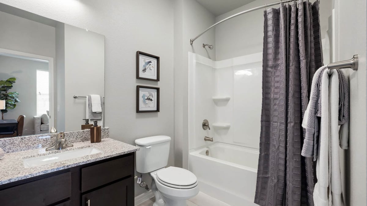Bathroom with a speckled granite vanity top over dark cabinets, a wall mirror, a toilet and a white tub with a curved shower rod