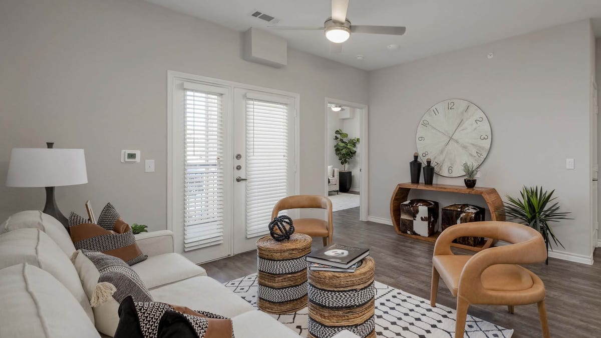 Furnished living room with gray wood-style flooring, a ceiling fan, a sofa and two chairs, and glass doors with blinds opening to a balcony
