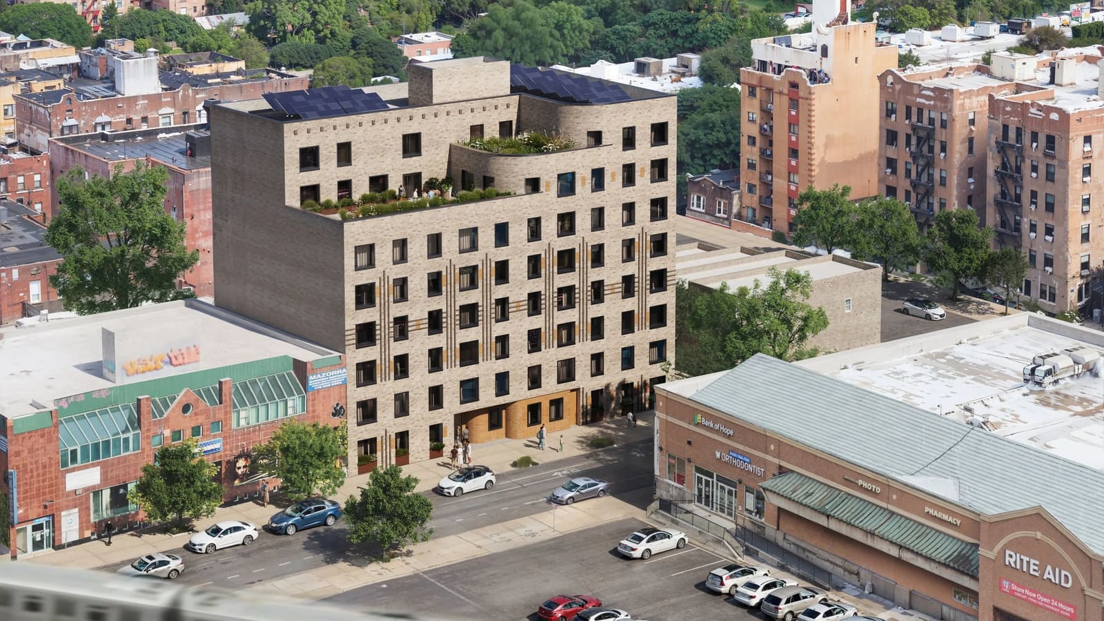 Rendering from above of a tan brick apartment building standing among older brick apartment houses and low stores, with solar panels on its roof, planted terraces on two curved setbacks where a few people stand, parked cars along the street in front, a parking lot and a store with a Rite Aid sign in the foreground and the blurred roof of a passing train at the bottom left