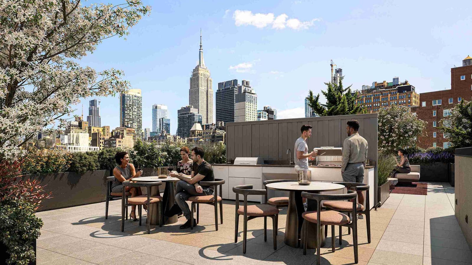 Rendering of a roof terrace with round dining tables, an outdoor kitchen with a grill, planters and flowering trees, and the Empire State Building in the distance