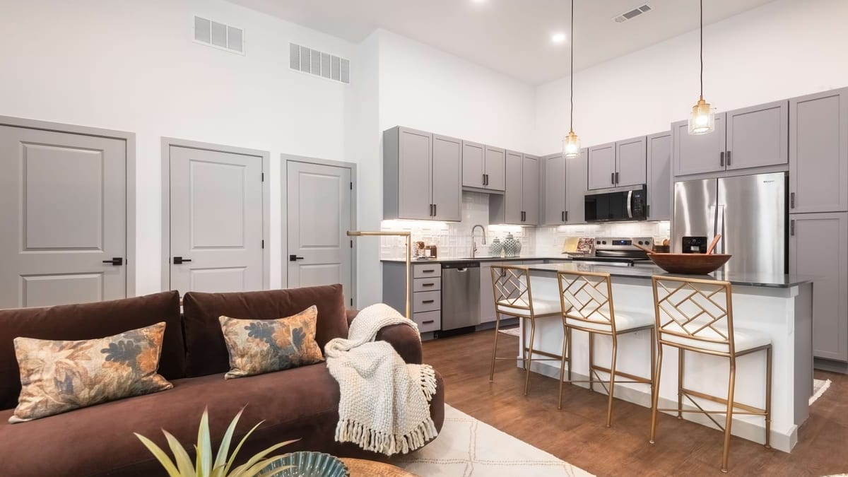 Living room with brown sofas open to a kitchen with grey cabinets and an island with three stools