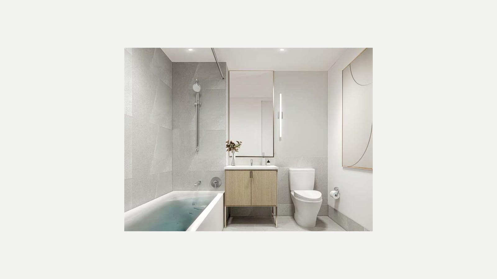Rendering of a bathroom with gray stone-look tile, a filled bathtub with a hand shower on a rail, a light wood vanity with a white sink under a mirror, a white toilet and a framed line drawing on the wall