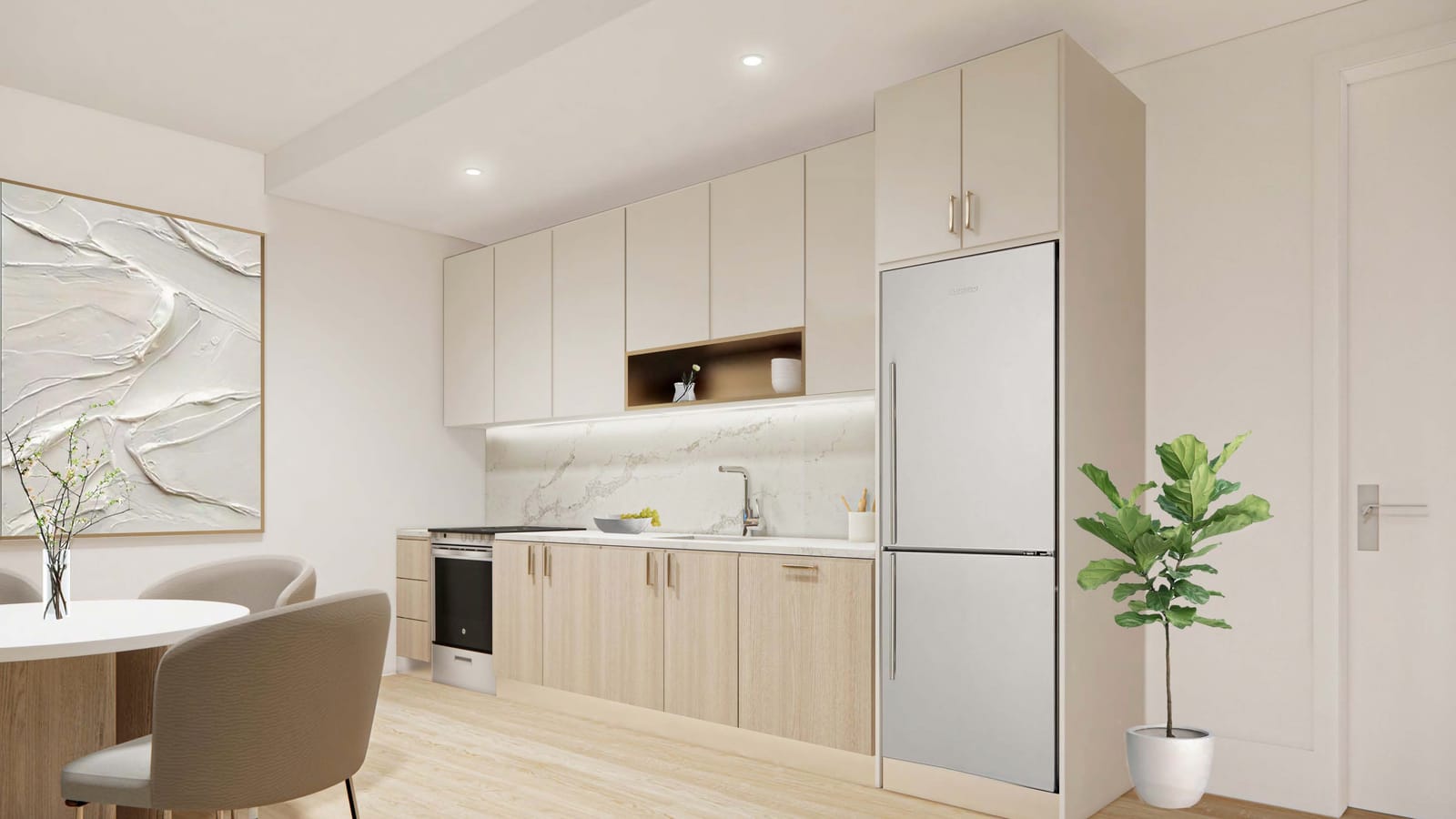 Rendering of an apartment kitchen along one wall with cream upper cabinets, light wood lower cabinets, a white stone backsplash, a stainless range with a flat cooktop, a sink, a tall stainless refrigerator, and a round white dining table with two chairs at left