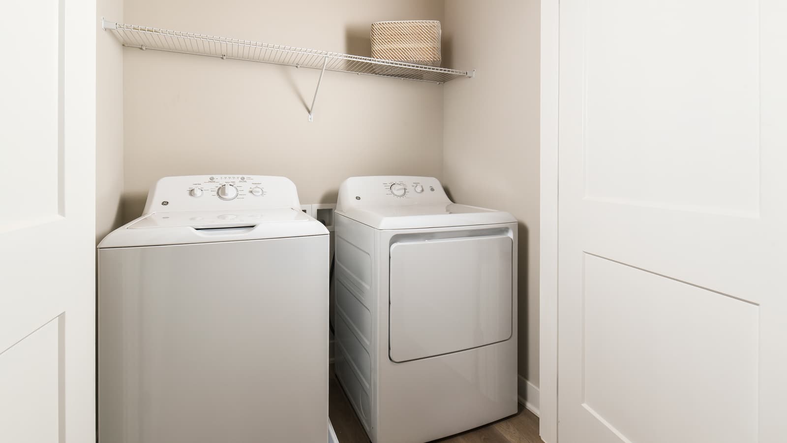 A white washer and dryer side by side in a closet with a wire shelf above