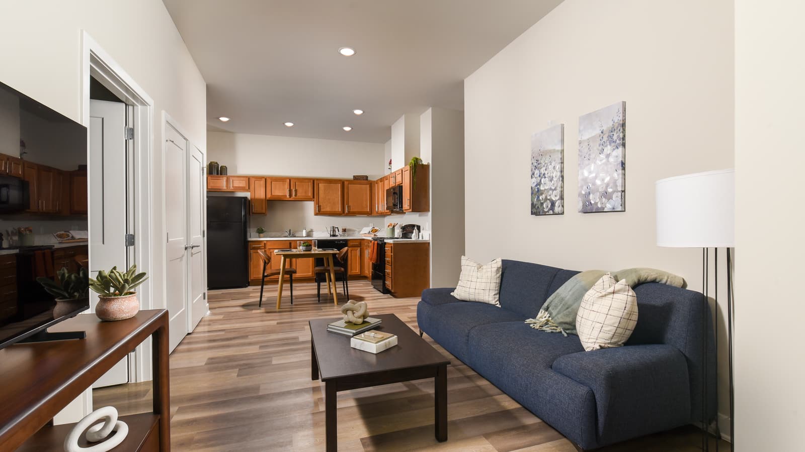 A living room with a navy sofa and a coffee table, open to a kitchen with wood cabinets and a small dining table