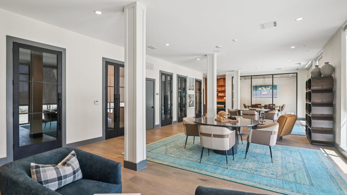 Lounge with dark blue armchairs, a blue patterned rug, glass-walled offices on the left and tables beyond