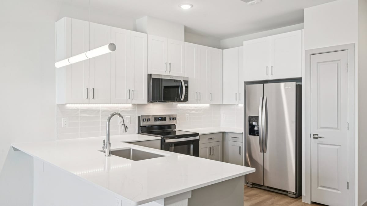 Unfurnished kitchen with white cabinets, white counters, a stainless-steel refrigerator, range, microwave and a peninsula with a sink