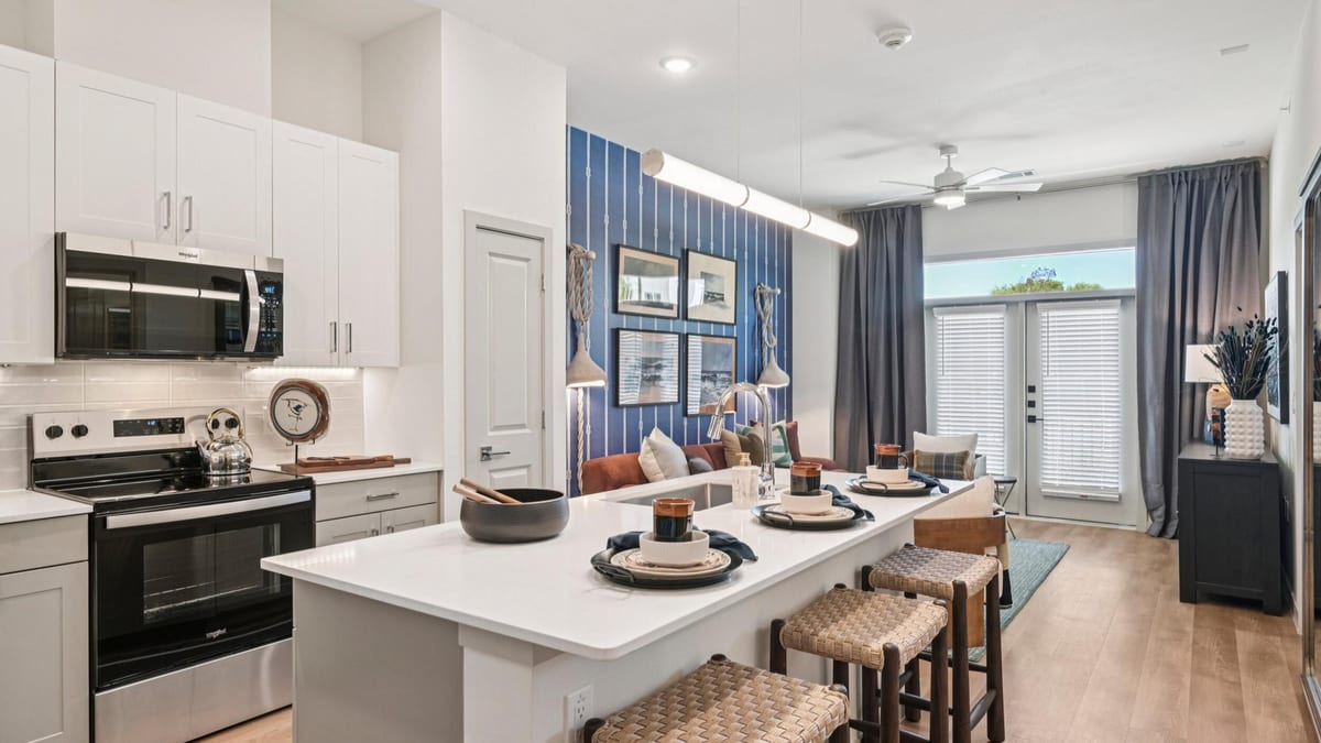 Open kitchen and living room with an island and woven stools, a red sofa, a blue accent wall and glass doors to a balcony