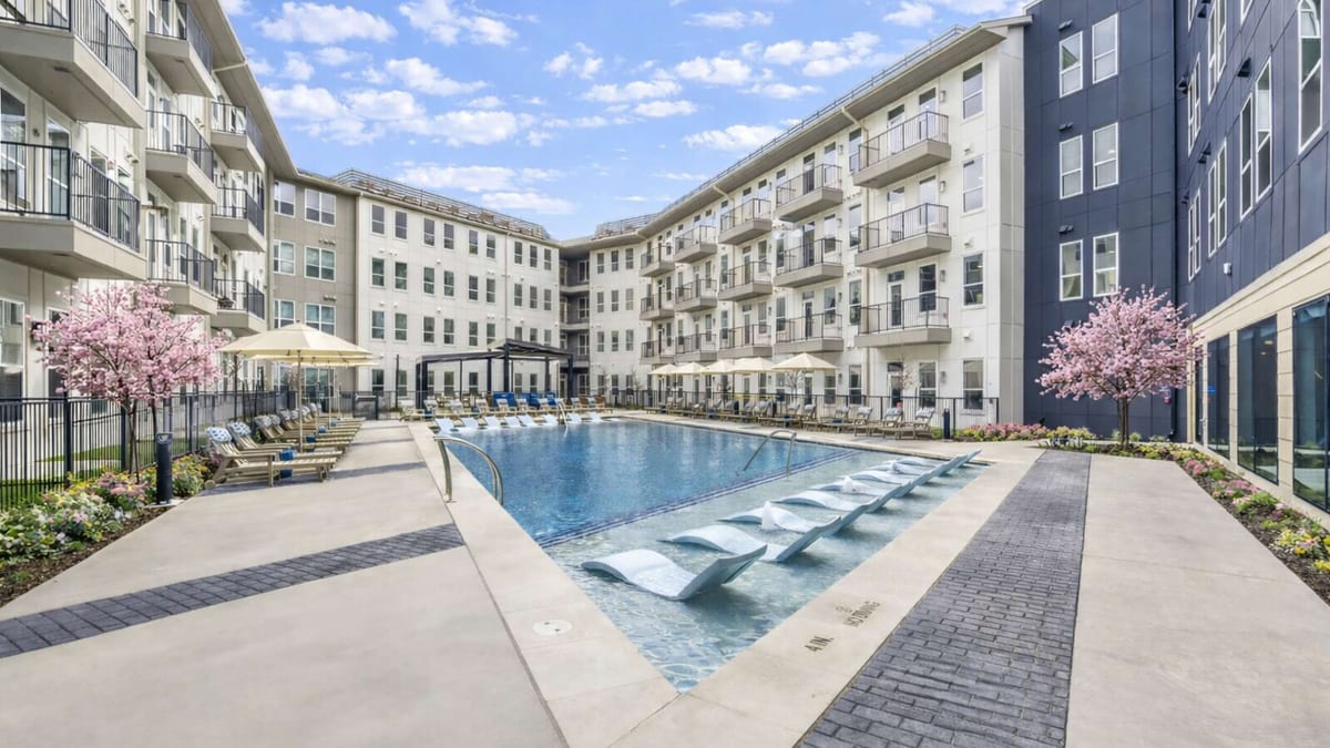 Long swimming pool with in-water loungers in a courtyard enclosed by four-story apartment wings with balconies