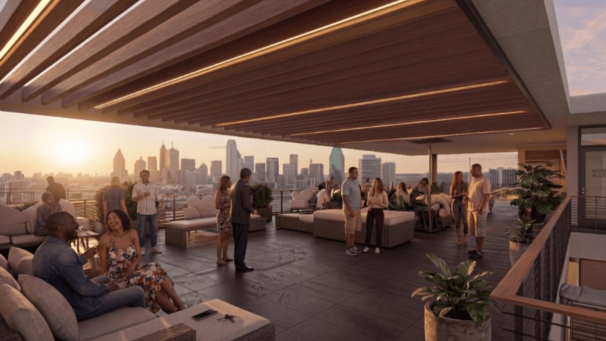 Rendering of a covered rooftop terrace with sofas, planters and people standing in groups, with a city skyline in the distance at sunset