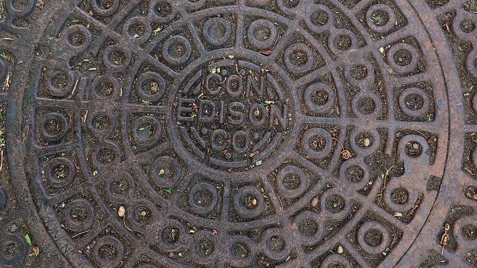 Close view of a round cast-iron manhole cover with the words Con Edison Co. cast in the centre, ringed by raised circles