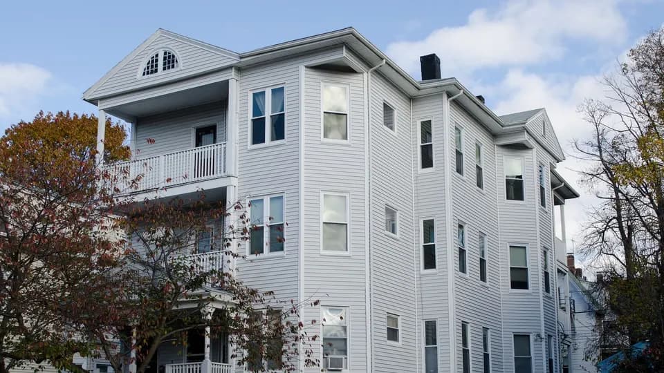 Three-story Worcester triple-decker with stacked front porches among autumn trees