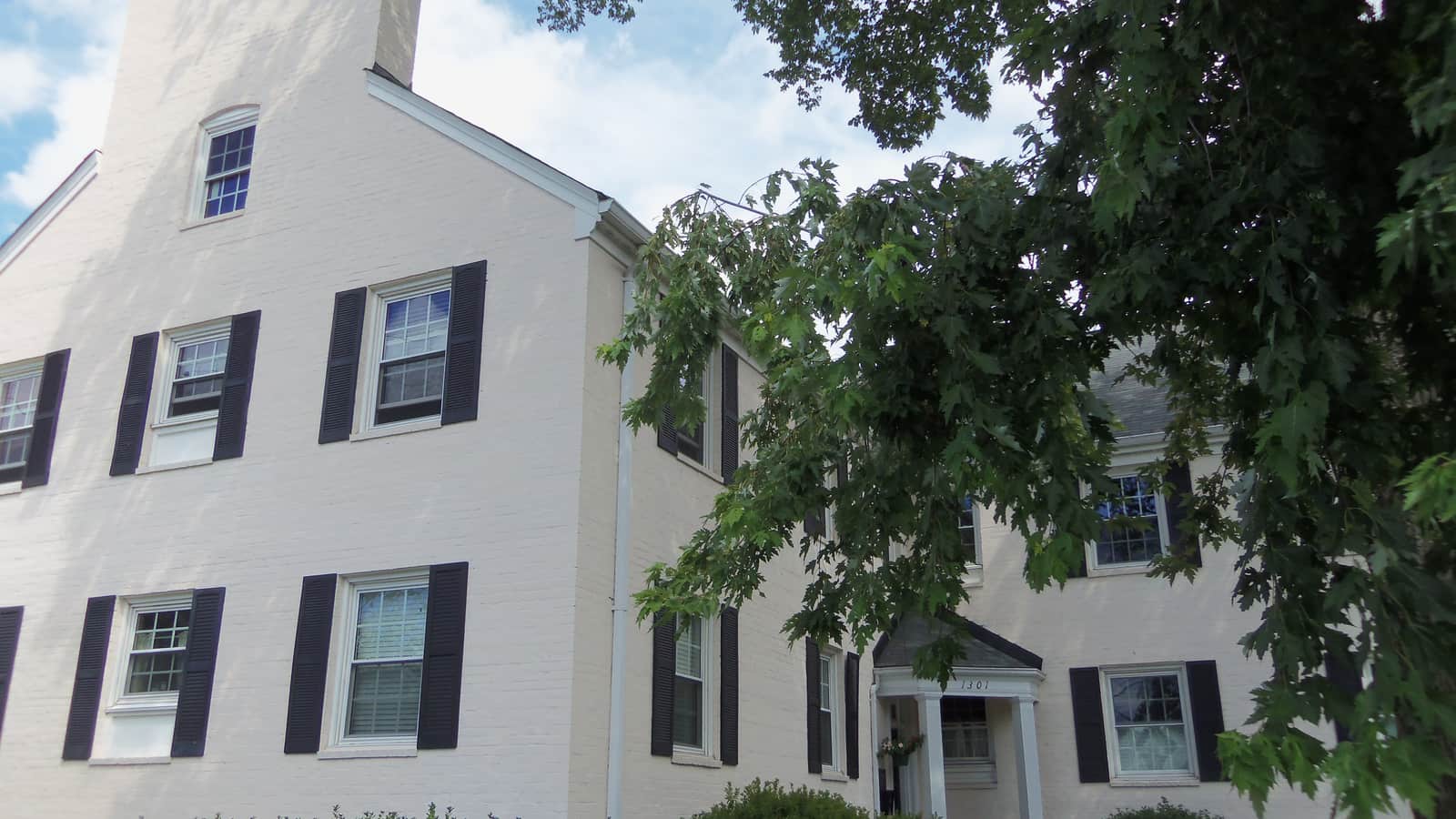 White-painted brick apartment facade with dark shutters, an entrance canopy and overhanging trees at Walter Reed Gardens in Arlington, Virginia.