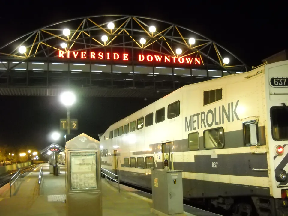 A Metrolink train under the Riverside Downtown station sign at night.
