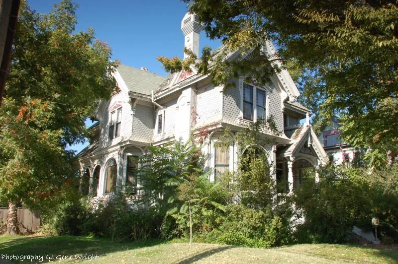 Steep-roofed white Newell Home behind trees and a lawn in Stockton